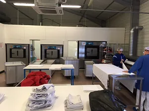 Spălătorie echipată Danube: trei mașini industriale montate în peretele despărțitor, mese cu rufe împăturite și doi angajați